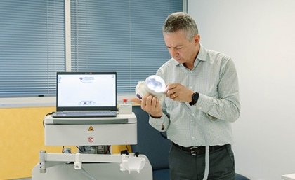 A man stands looking at an ultrasound machine in a hospital room or clinical setting. 